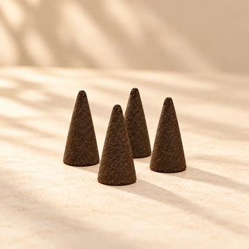 Four dark brown hand-dipped incense cones with rounded tips on a warm neutral background.
