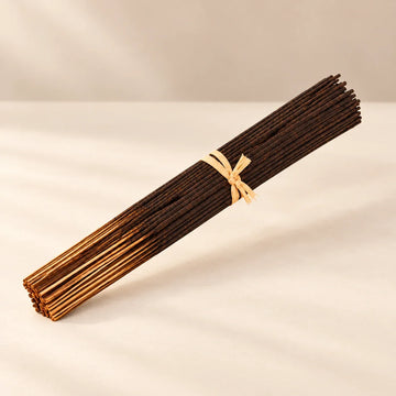 Bundle of dark brown hand-dipped incense sticks with bamboo ends on a warm ivory background.