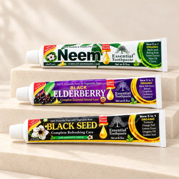 Neem, Elderberry, and Black Seed toothpaste tubes on soft ivory stone steps