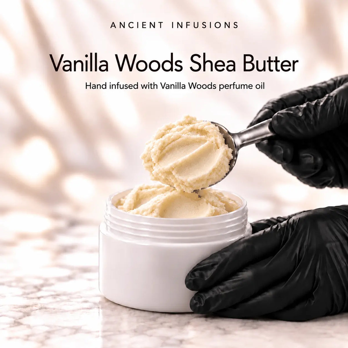 Black vinyl-gloved hands scoop raw shea butter hand infused with Vanilla Woods perfume oil.