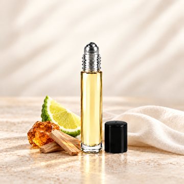 Slim glass perfume oil bottle with a silver roller top and black cap beside amber-colored resin, sandalwood and bergamot.