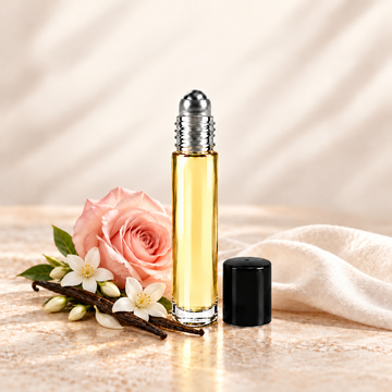 Slim glass perfume oil bottle with a silver roller top and black cap beside blush rose, jasmine and vanilla.