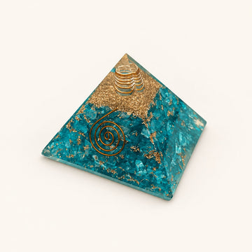 Aquamarine Orgone Pyramid with aqua-blue aquamarine chips and metallic details on a warm ivory background
