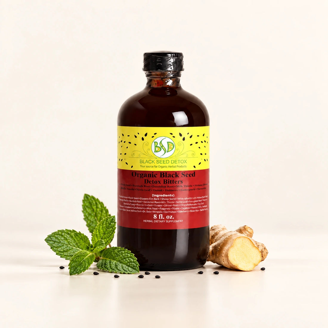 Black Seed Detox Bitters bottle with ginger, spearmint and black seeds on a soft ivory background.