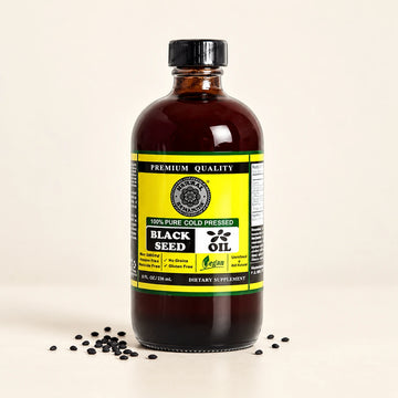 Black Seed Oil bottle with black seeds resting on an ivory surface.