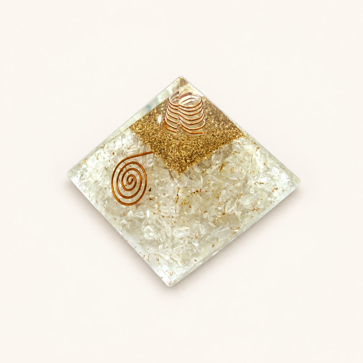 Clear Quartz Orgone Pyramid with translucent clear quartz chips and metallic details on a warm ivory background