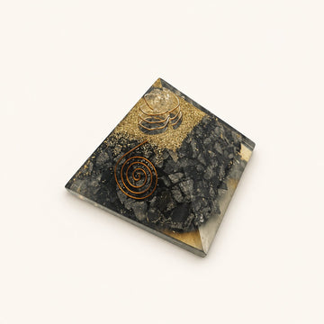 Hematite Orgone Pyramid with dark metallic-gray hematite chips and metallic details on a warm ivory background