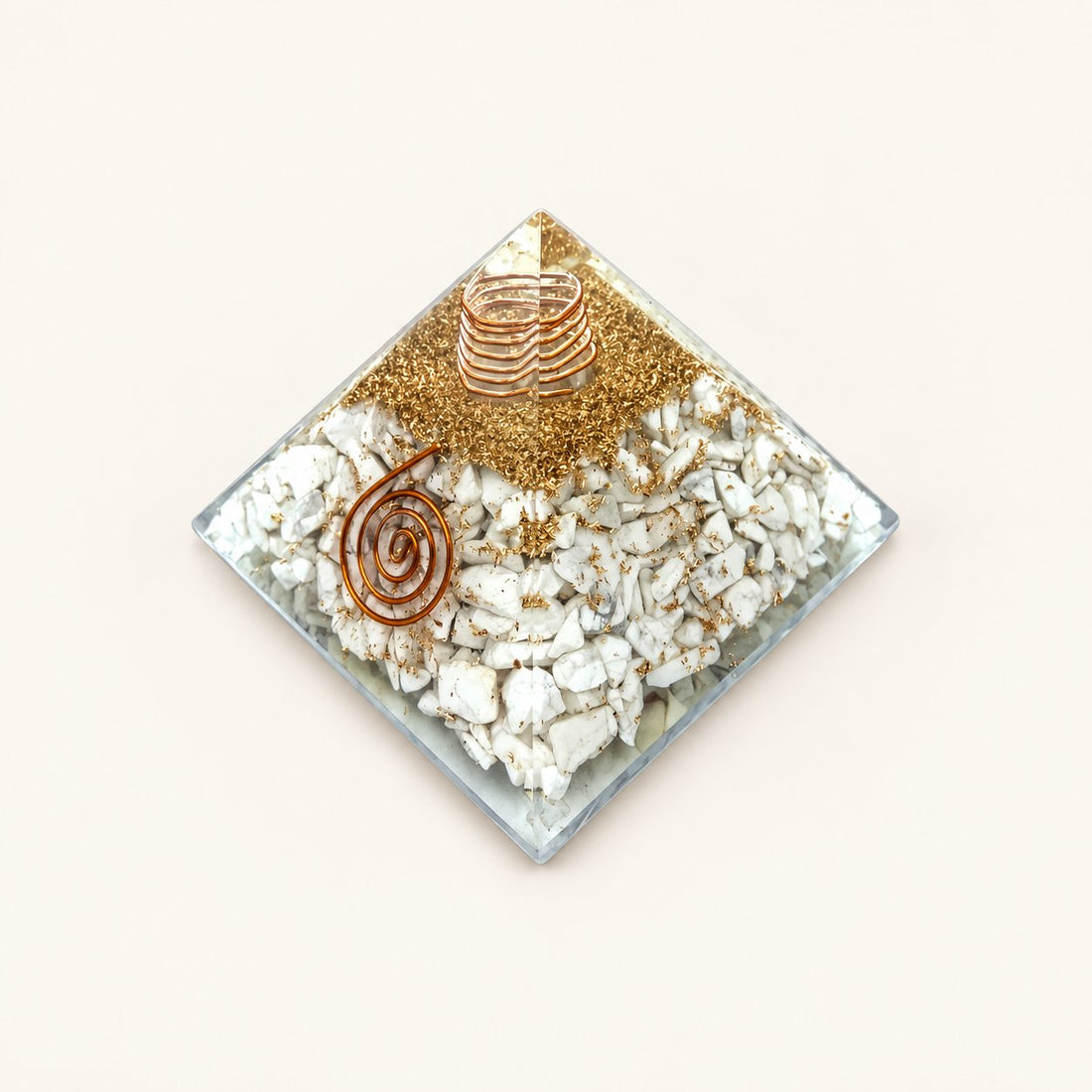 Howlite Orgone Pyramid with white howlite chips with gray veining and metallic details on a warm ivory background