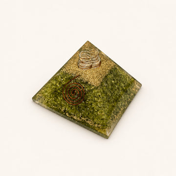Peridot Orgone Pyramid with olive-green peridot chips and metallic details on a warm ivory background