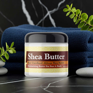 Barack Obama Inspired Scented Shea Butter on a marble surface with blue towels and green leaves.