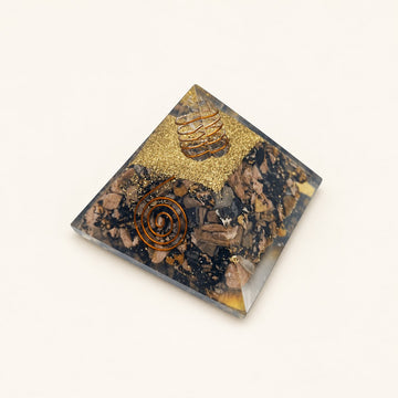 Rhodonite Orgone Pyramid with muted pink and charcoal rhodonite chips and metallic details on a warm ivory background