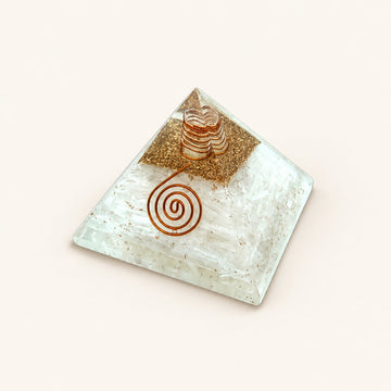 Selenite Orgone Pyramid with translucent white selenite chips and metallic details on a warm ivory background