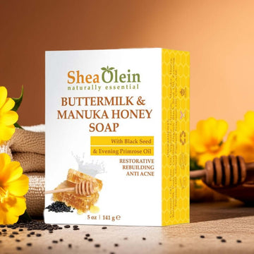 Shea Olein Buttermilk & Manuka Honey Soap with upright box, black seeds, primrose oil, and honeycomb on a warm-toned counter – restorative and anti-acne bar.
