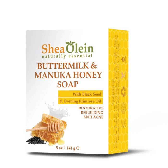 Shea Olein Buttermilk & Manuka Honey Soap with upright box, black seeds, primrose oil, and honeycomb on a warm-toned counter – restorative and anti-acne bar.
