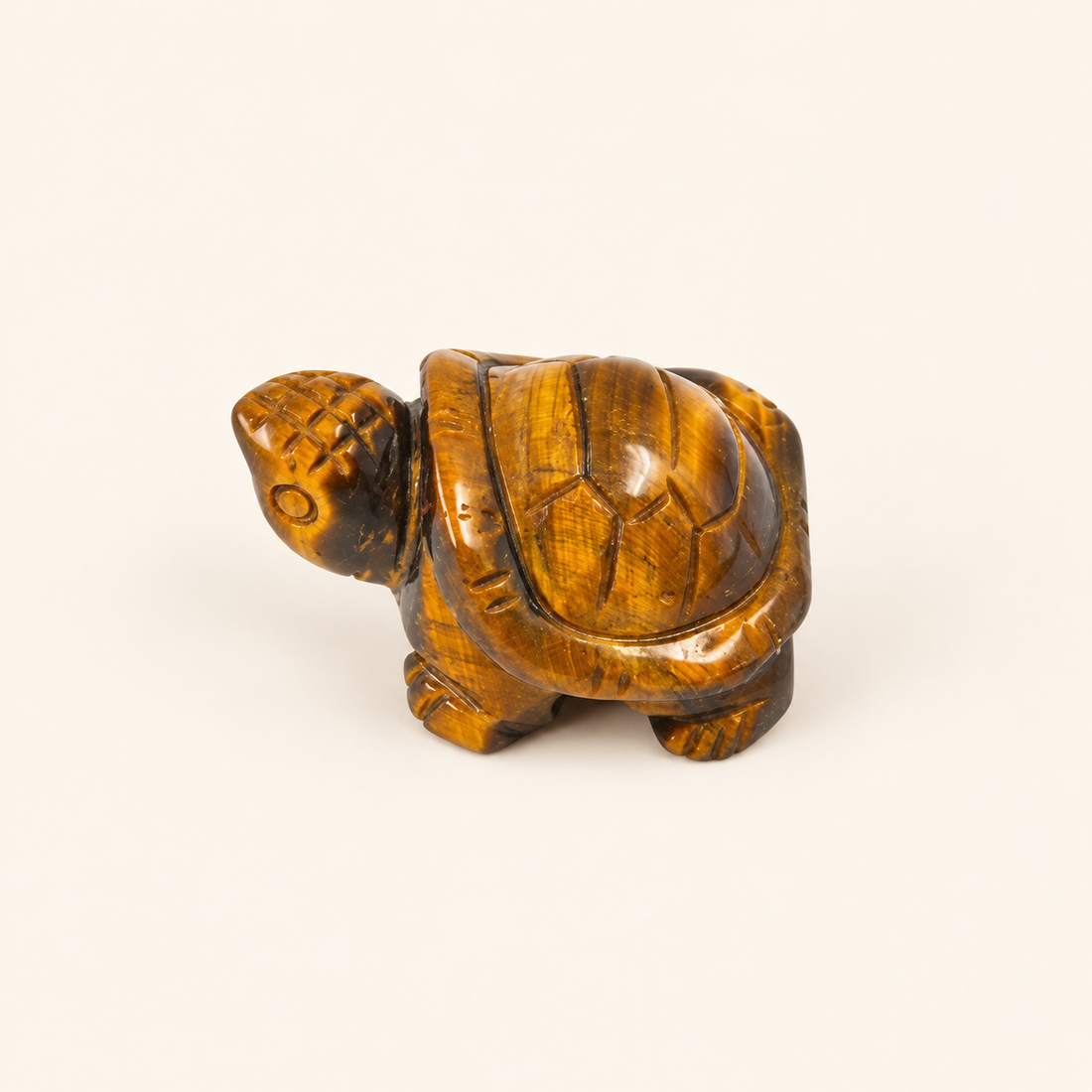 Tiger's Eye Carved Turtle with golden-brown bands and a reflective sheen on a soft ivory background