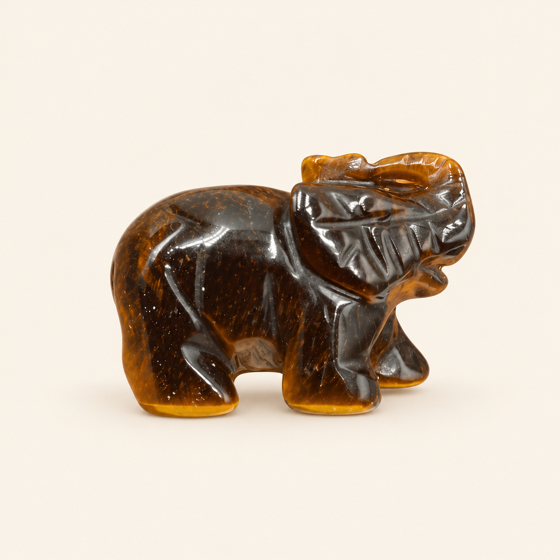 Tiger's Eye Carved Elephant with golden-brown bands and a reflective sheen on a soft ivory background