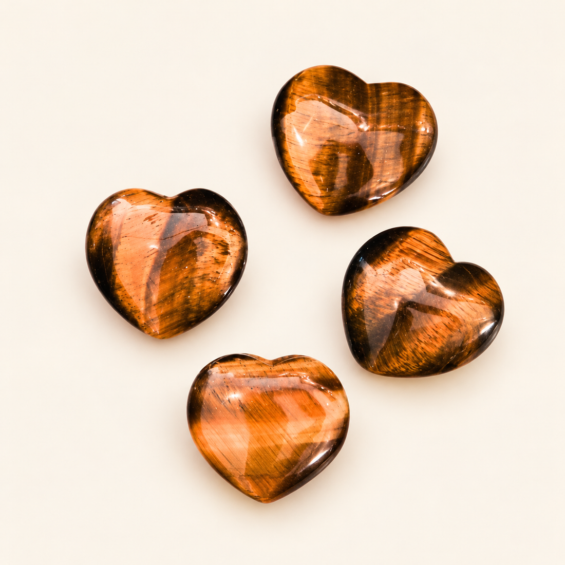 Tiger's Eye Carved Heart with golden-brown bands and a reflective sheen on a soft ivory background