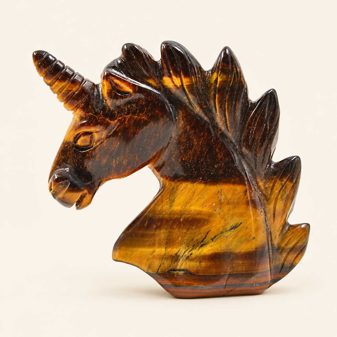 Tiger's Eye Carved Unicorn with golden-brown bands and a reflective sheen on a soft ivory background
