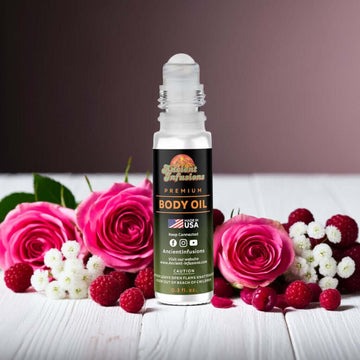 Bottle of Bath & Body Works You Are the One Inspired Body Oil surrounded by pink roses and berries on a white wooden table.